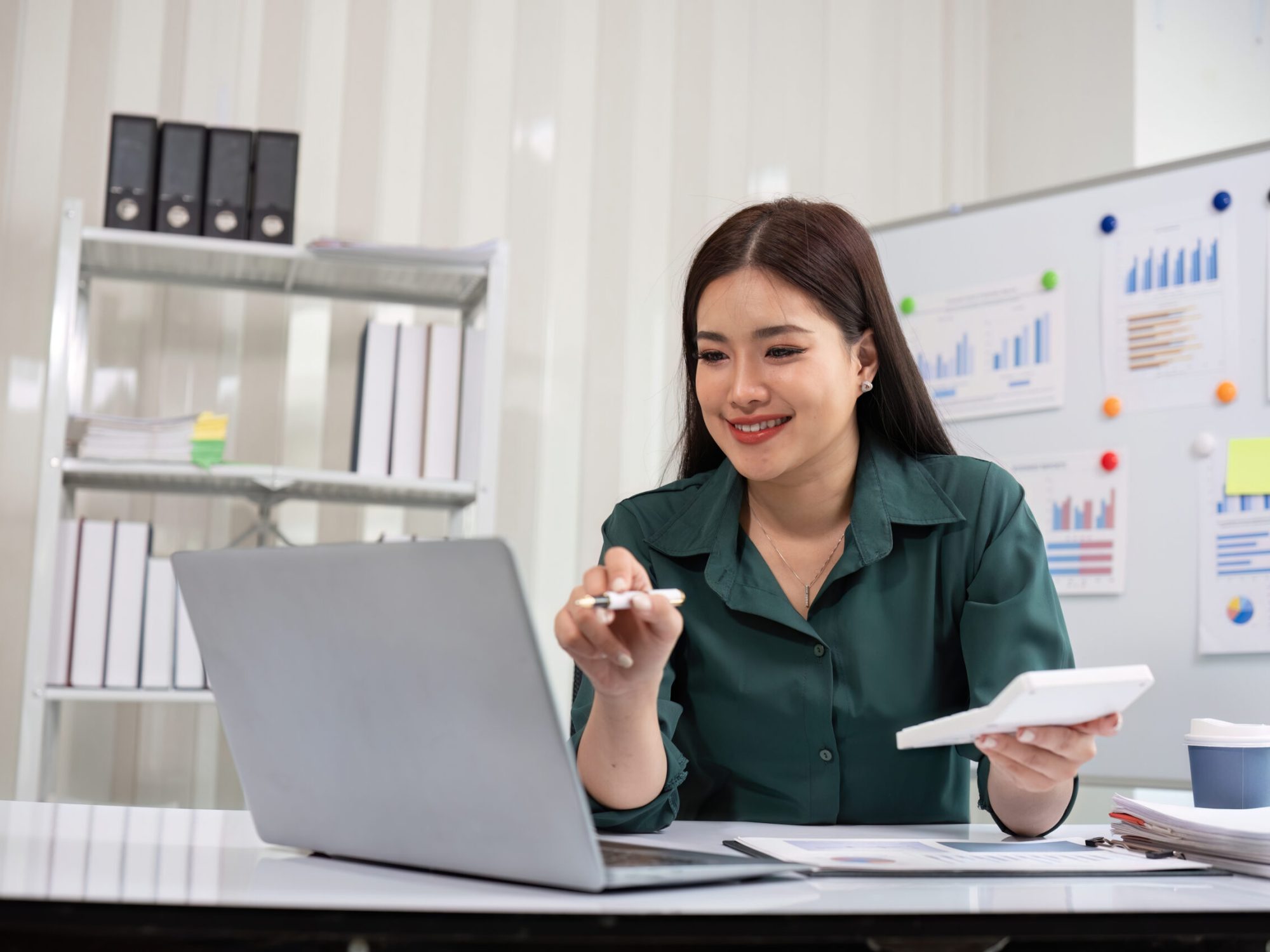 A young accountant working diligently on financial documents using a laptop in a modern office environment, surrounded by charts and graphs.